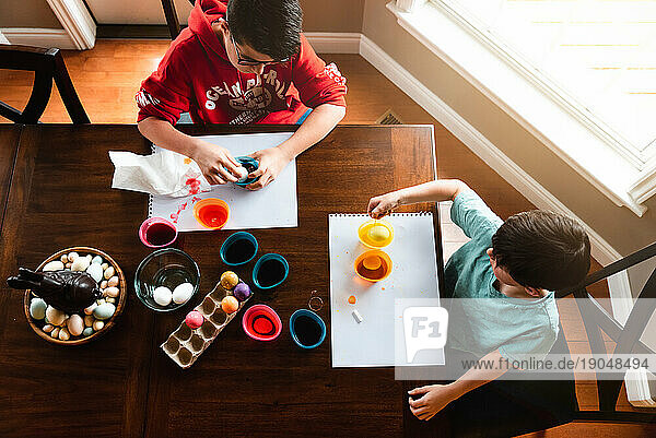 High angle shot of two boys dying colorful Easter eggs at table.