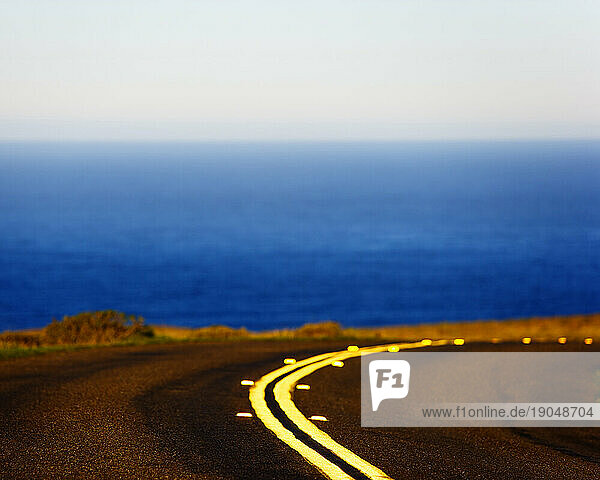 Low angle view of road  double yellow line  right turn  and ocean horizon line.