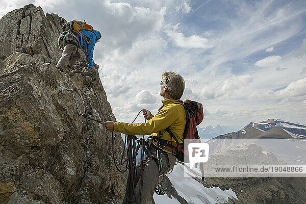 Mountaineer belays teammate on summit ridge