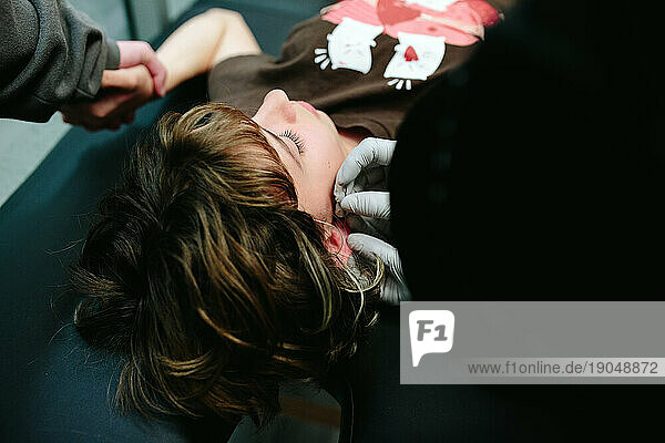 Closeup of a piercer putting the needle through a teen girl's earlobe