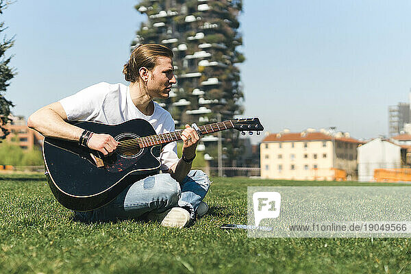 Young white singer play the guitar in a garden during a sunny day