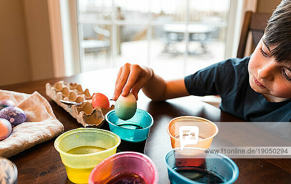 Boy dipping an egg in a container of dye to color it for Easter.