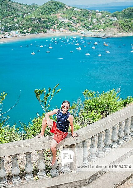 Porträt von Tourist Mann in der Ansicht der Bucht von San Juan del Sur. Happy Tourist sitzt in einem Aussichtspunkt einer Bucht  Reisen und Tourismus Promotion Konzept