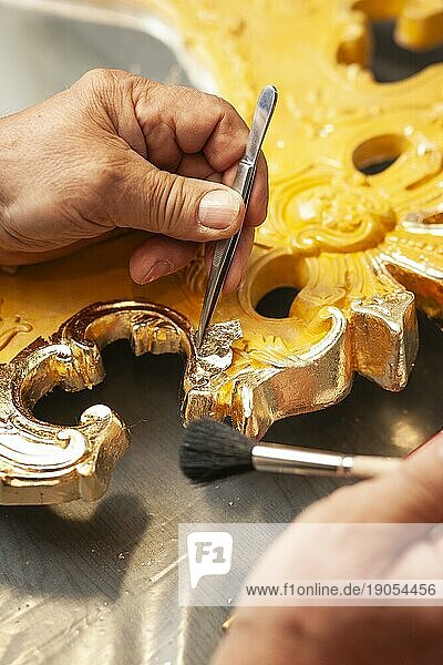Detail eines mit Blattgold vergoldeten Spiegels  ein Mann legt ein Stück Blatgold mit einer Pinzette ab und streicht mit einem Pinsel darüber