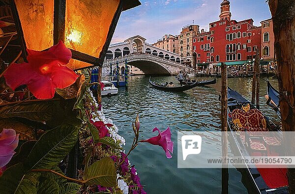 Die berühmte Rialtobrücke oder Ponte di Rialto über den Canal Grande  Venedig  Italien. Ikonisches Reiseziel der UNESCO Welterbestadt. Vorbeifahrende oder vertäute Gondeln  beleuchtete Laterne. Bunte Renaissancefassaden von Gebäuden am Wasser. Selektiver Fokus