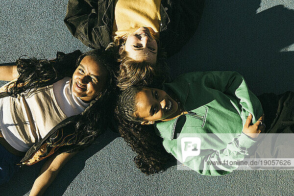 Blick von oben auf lächelnde  am Boden liegende Freundinnen an einem sonnigen Tag