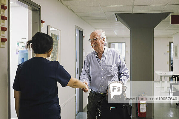 Lächelnder älterer Mann  der weibliches medizinisches Personal im Krankenhaus begrüßt
