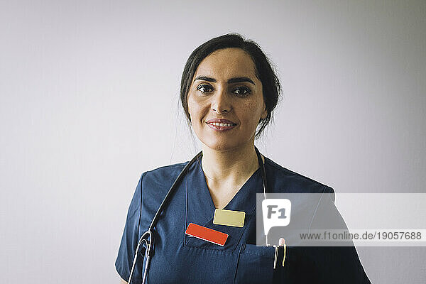 Porträt einer lächelnden Mitarbeiterin im Gesundheitswesen vor einer weißen Wand