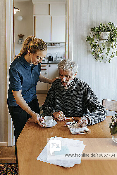 Weibliche Pflegehelferin serviert Tee für einen älteren Mann  der zu Hause sitzt