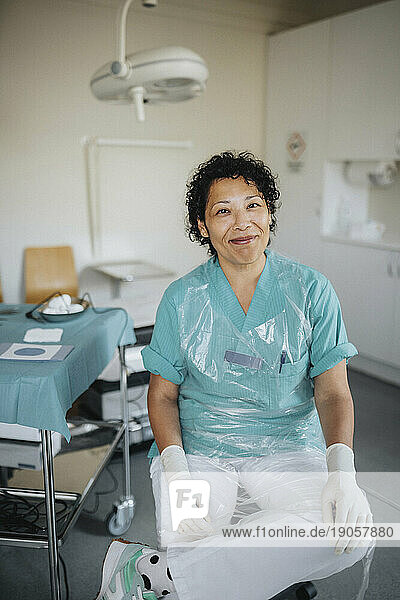 Porträt einer lächelnden Ärztin in Uniform  die in einem medizinischen Untersuchungsraum sitzt