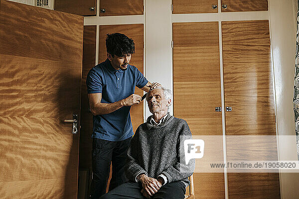 Männliche Pflegekraft  die sich um einen älteren Mann kümmert  der zu Hause sitzt