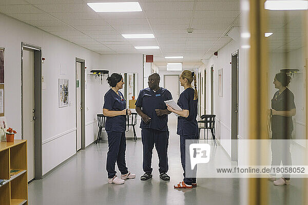 Männliches und weibliches medizinisches Personal diskutieren zusammen  während sie auf dem Flur eines Krankenhauses stehen