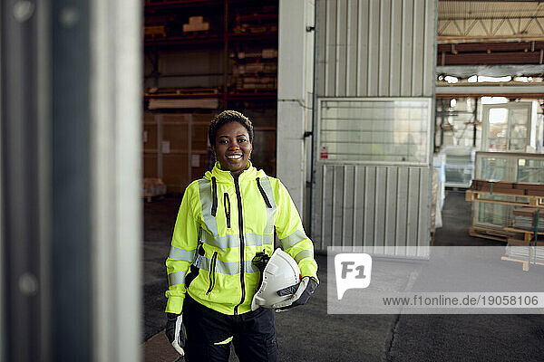 Porträt eines lächelnden Arbeiters in Arbeitsschutzkleidung mit Schutzhelm in einer Fabrik