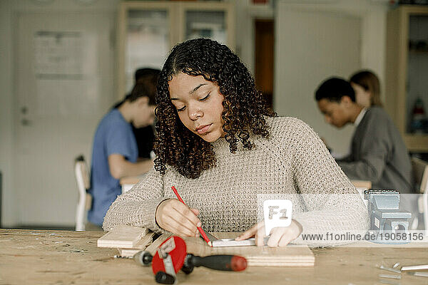 Konzentrierte Schülerin mit lockigem Haar  die während des Tischlerkurses auf Holz markiert