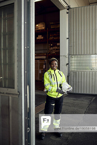Porträt einer lächelnden jungen Arbeiterin in Arbeitskleidung  die in einer Fabrik steht