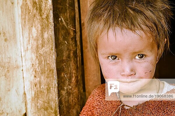 Dolpo  Nepal  ca. Mai 2012: Kleines Mädchen mit braunen glitzernden Augen in rotem Pullover lehnt an der Tür in Dolpo  Nepal. Dokumentarischer Leitartikel  Asien