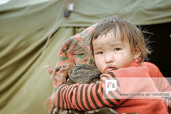 Dolpo  Nepal  ca. Juni 2012: Kleines braunhaariges Mädchen in schwarz rot gestreiftem Hemd umarmt ihre Mutter und schaut mit braunen Augen traurig in die Kamera in Dolpo  Nepal. Dokumentarischer Leitartikel  Asien