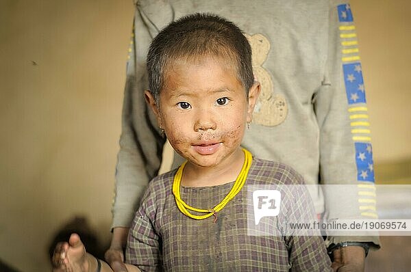 Dolpo  Nepal  ca. Mai 2012: Kleines braunäugiges Mädchen in kariertem Hemd trägt gelbe Perlen und schaut freundlich in die Kamera in Dolpo  Nepal. Dokumentarischer Leitartikel  Asien