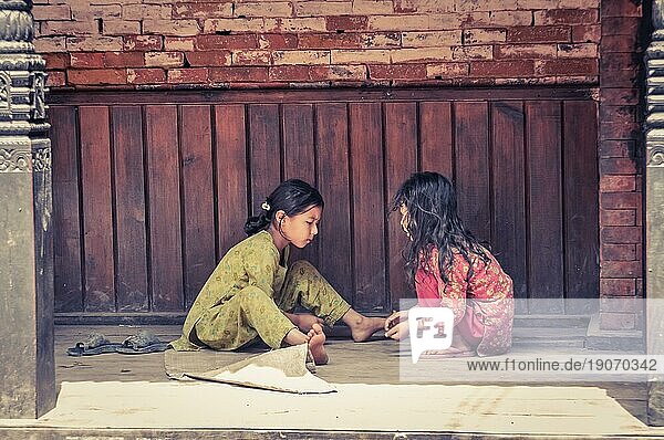 Bhaktapur  Nepal  ca. Juni 2012: Zwei junge Mädchen mit langen schwarzen Haaren sitzen draußen auf dem Boden und spielen Spiele in Bhaktapur  Nepal. Dokumentarischer Leitartikel  Asien