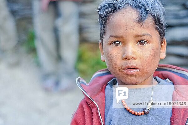Dolpo  Nepal  etwa im Mai 2012: Ein Junge mit braunen Haaren und Augen hat Schmutz auf den Wangen und trägt Perlen und ein graues Hemd mit rotem Sweatshirt in Dolpo  Nepal. Dokumentarischer Leitartikel  Asien