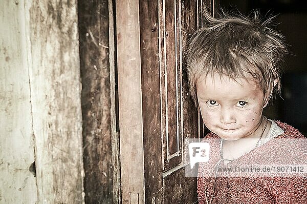 Dolpo  Nepal  ca. Mai 2012: Kleines schüchternes Mädchen in rotem Pullover lehnt an der Tür und schaut neugierig mit braunen Augen in die Fotokamera in Dolpo  Nepal. Dokumentarischer Leitartikel  Asien