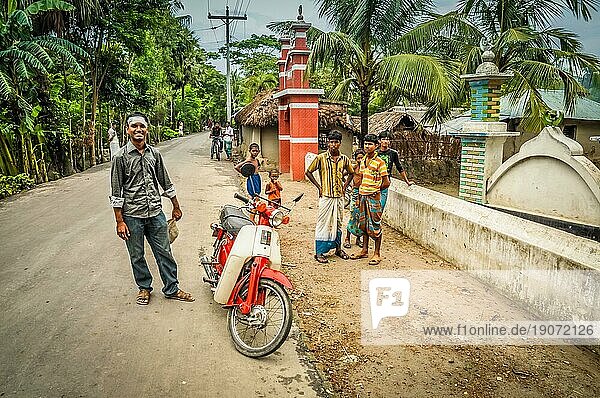 Paigacha  Bangladesch  etwa im Juli 2012: Junge einheimische Jungen stehen mit einem weiß roten Motorrad auf der Straße und lächeln in die Kamera in Paigacha  Bangladesch. Dokumentarischer Leitartikel  Asien