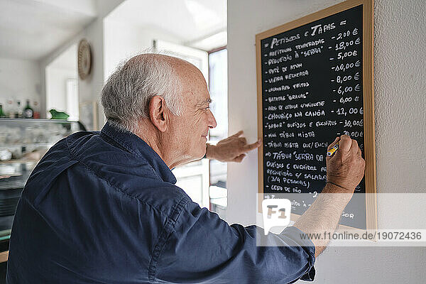 Smiling cafe owner writing menu on black board with pen