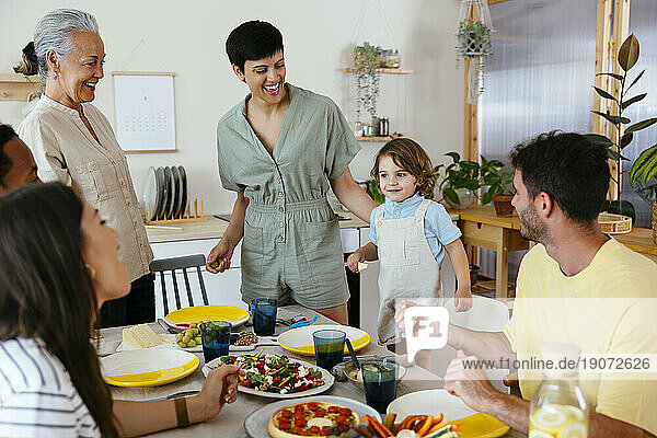 Smiling family talking to boy near dining table at kitchen