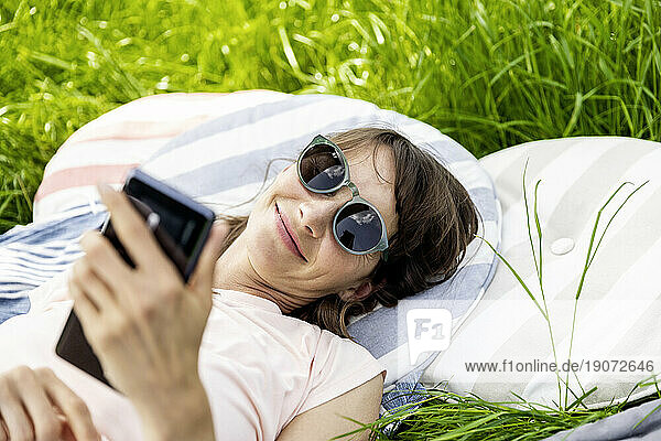 Relaxed woman lying on a meadow using cell phone