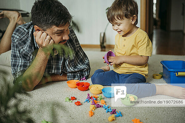 Smiling father and son playing with plastic toys at home