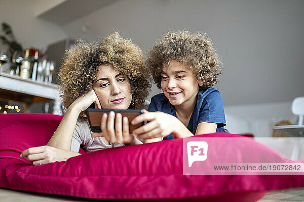 Mother and son watching a video on smartphone  lying on big pillow