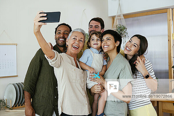 Cheerful family taking selfie with smart phone in kitchen