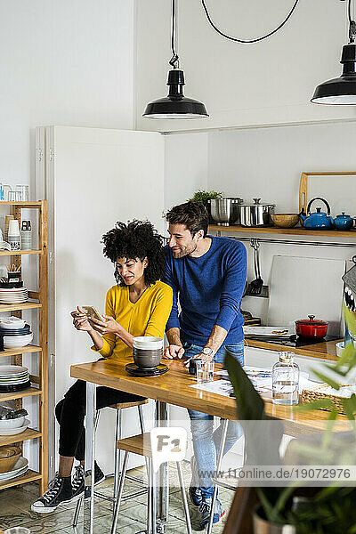 Couple in kitchen at home sharing cell phone