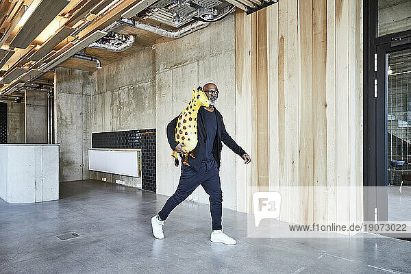 Mature businessman holding giraffe figurine walking in modern office