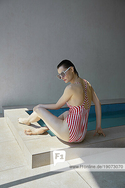 Young woman wearing striped swimwear sitting by hot tub