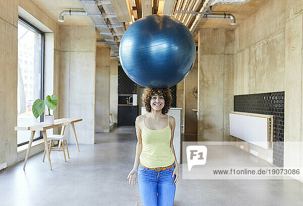 Portrait of smiling woman balancing a fitness ball on her head