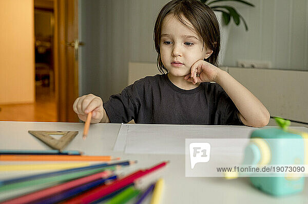 Thoughtful boy with colored pencils on table at home