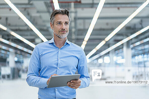Confident businessman with tablet in a factory hall