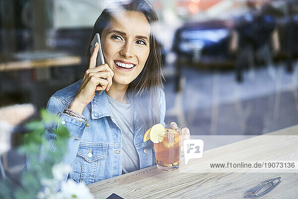 Smiling young woman on the phone drinking tea in cafe