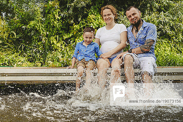 Happy pregnant mother with family splashing water on footbridge over lake