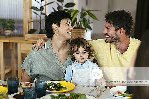 Smiling parents with son having lunch on dining table at home
