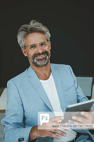 Smiling businessman holding tablet PC sitting at office