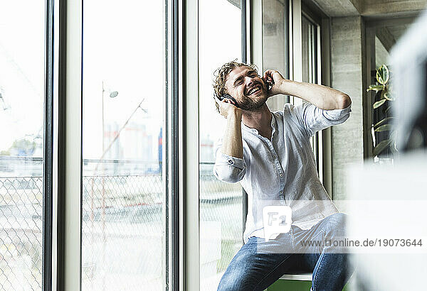 Happy casual young man listening to music with headphones at the window