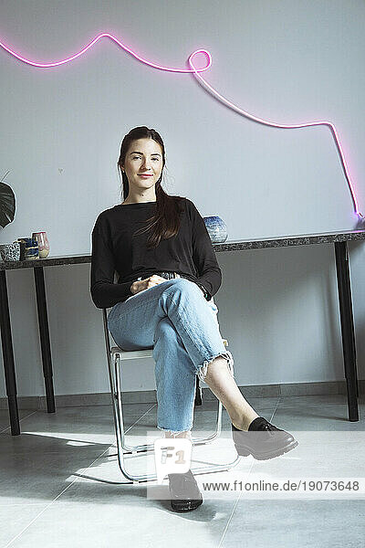 Smiling confident artist sitting on chair in front of wall at workshop