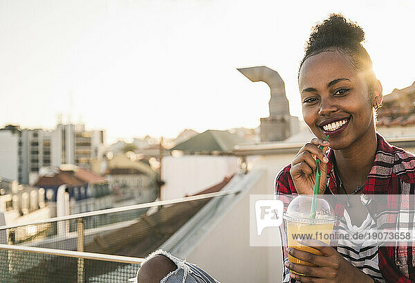 Portrait of happy young woman having a drink on rooftop at sunset