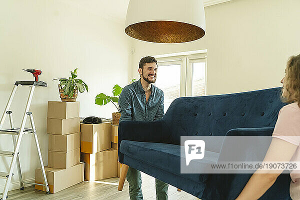 Smiling man carrying sofa with help of girlfriend at home