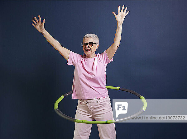 Senior woman practicing hula hoop against blue background