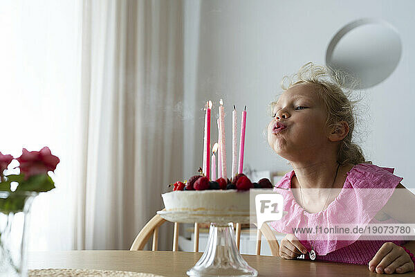 Blond girl blowing birthday candles at home