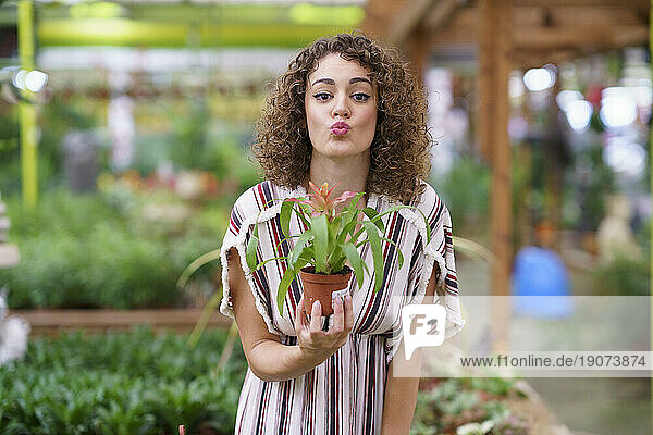 Woman puckering lips holding plant standing at nursery