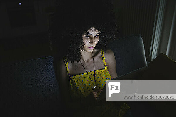 Young woman using her digital tablet in the night on the sofa